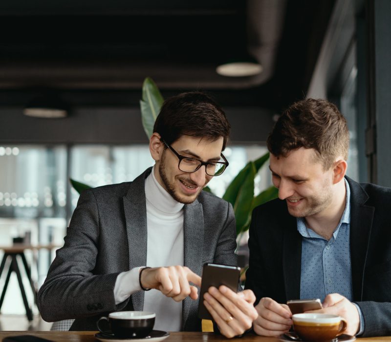 One-on-one meeting. Two young business people sitting at table in restaurant having a conversation using a phone and having a coffee. Businessman using a smartphone